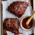 Overhead image of baby back ribs with gochujang glaze on a parchment lined baking sheet.