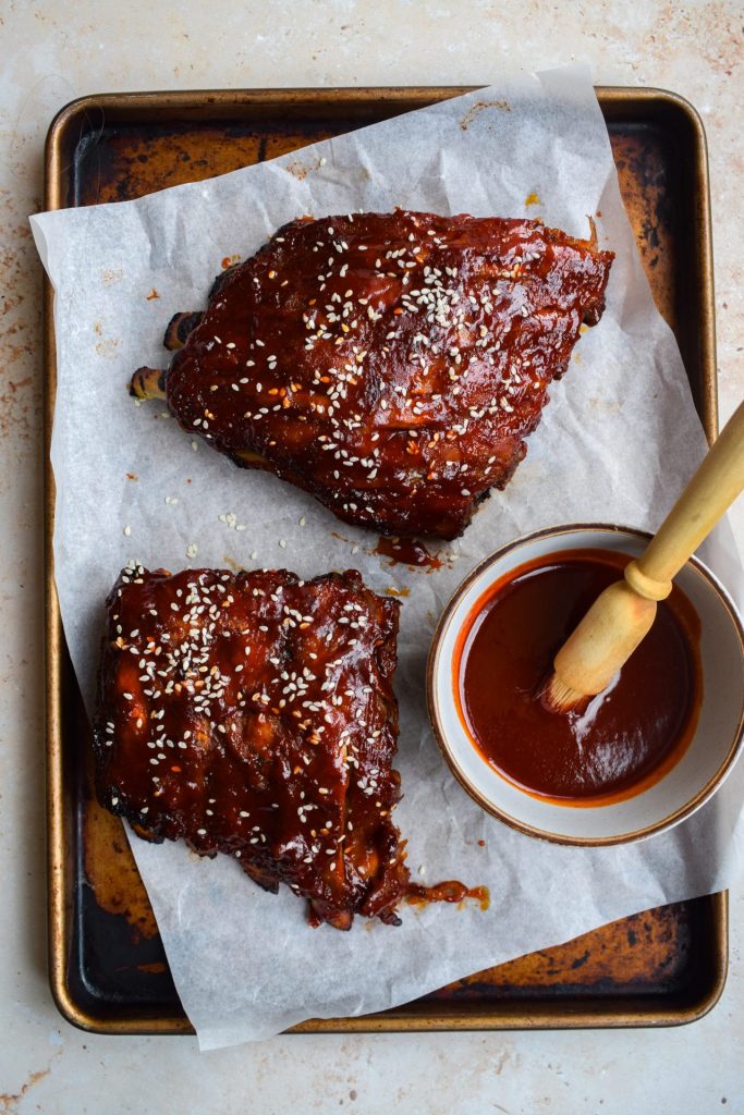 Overhead image of baby back ribs with gochujang glaze on a parchment lined baking sheet.