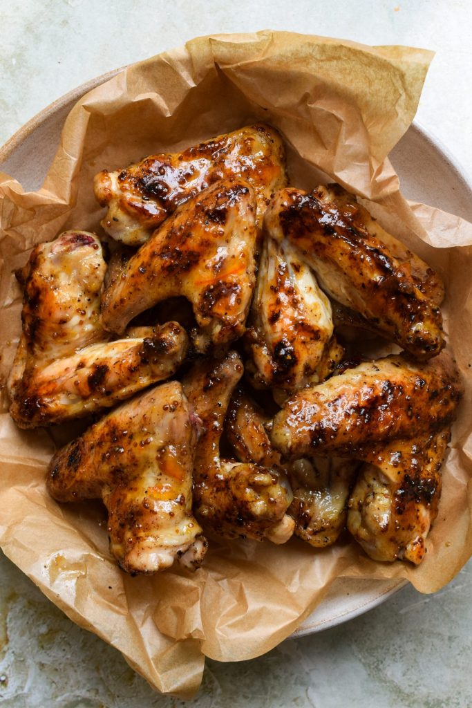 Baking parchment-lined plate of sticky marmalade and wholegrain mustard wings.