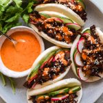 Place of loaded pork bao buns with cucumber, radish and a pot of creamy gochujang drizzle.