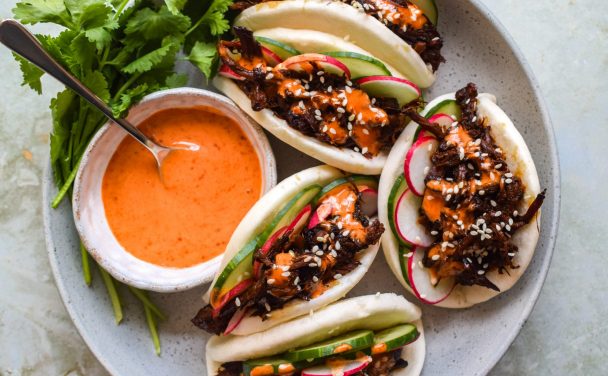 Place of loaded pork bao buns with cucumber, radish and a pot of creamy gochujang drizzle.