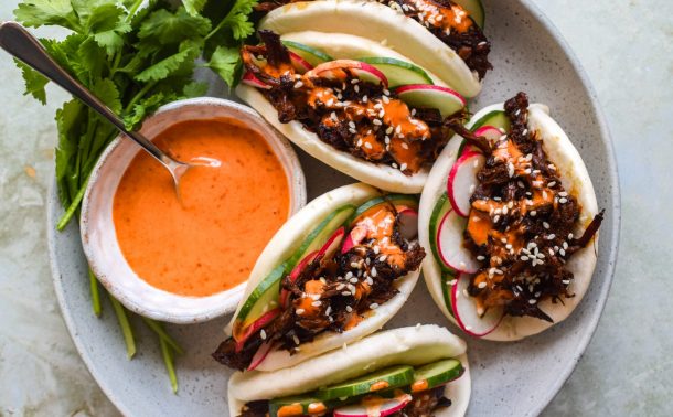 Place of loaded pork bao buns with cucumber, radish and a pot of creamy gochujang drizzle.
