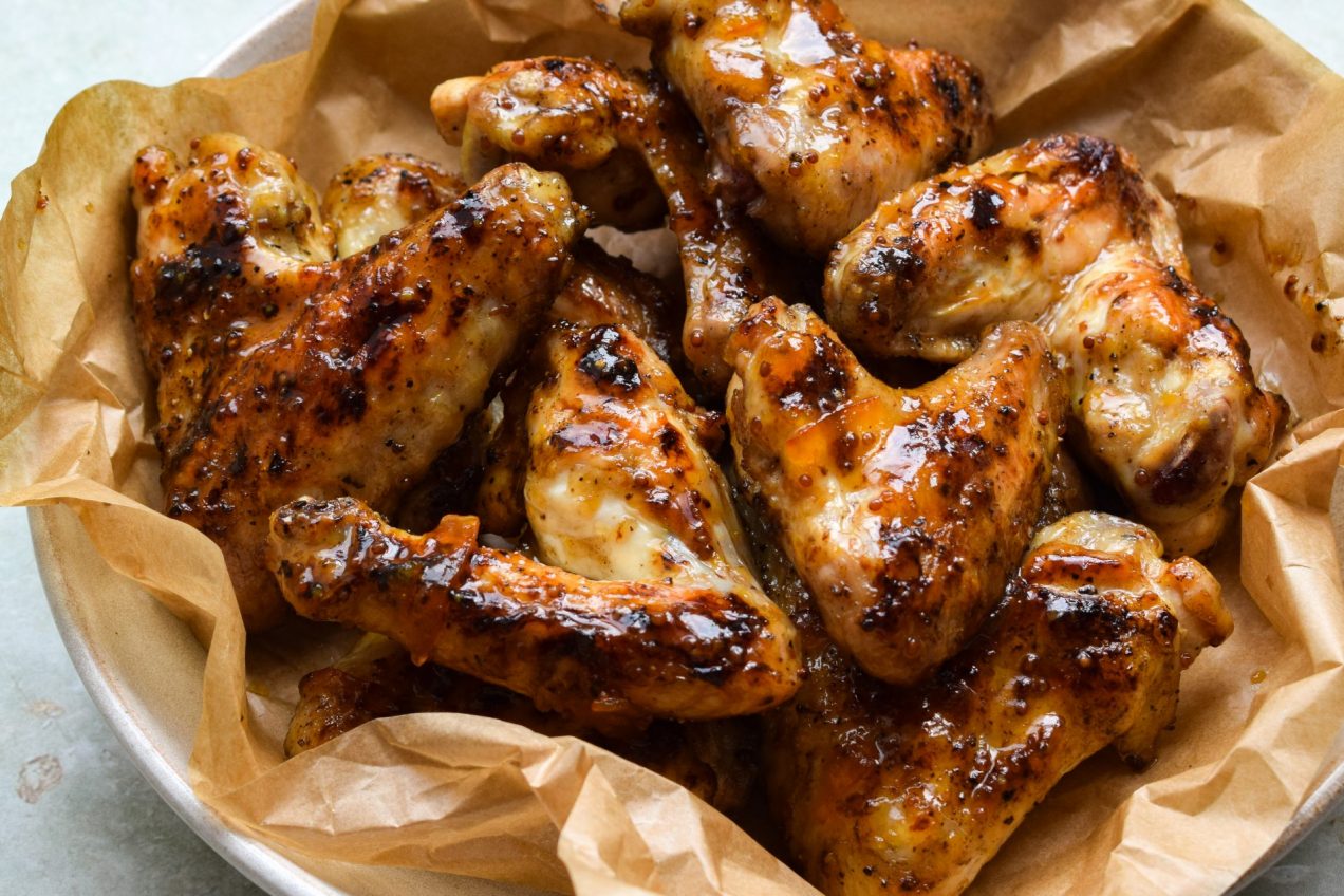 Marmalade and wholegrain mustard glazed chicken wings on a parchment lined plate.