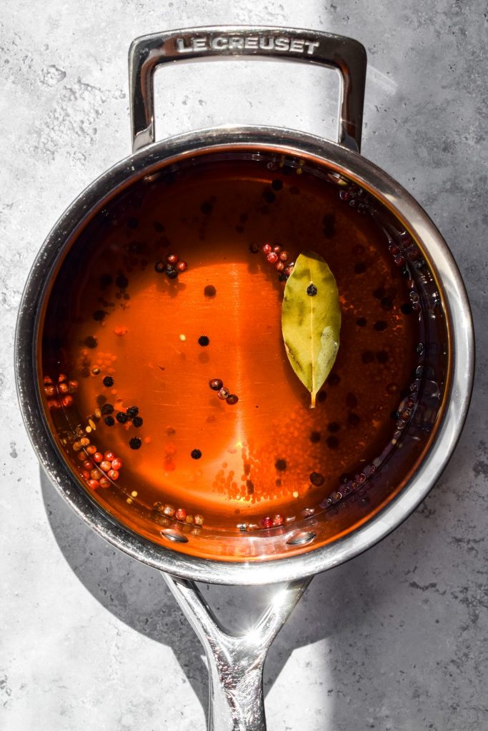Pickling liquid with peppercorns, bay leaf and mustard seeds in a silver saucepan.