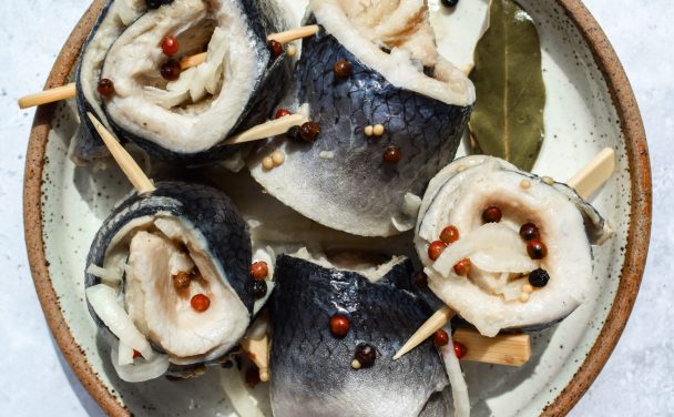 Plate of herring rollmops alongside some of their pickling spices.