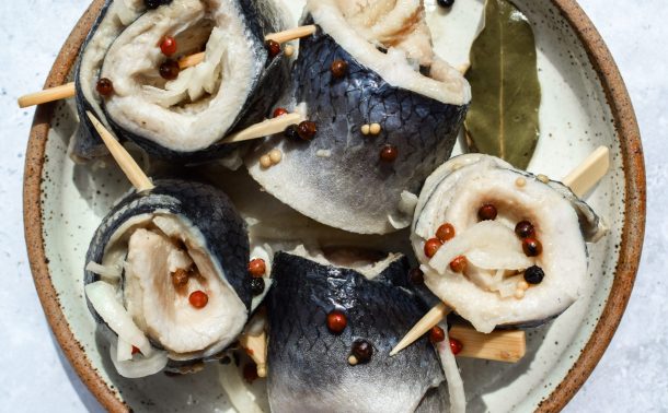 Plate of herring rollmops alongside some of their pickling spices.