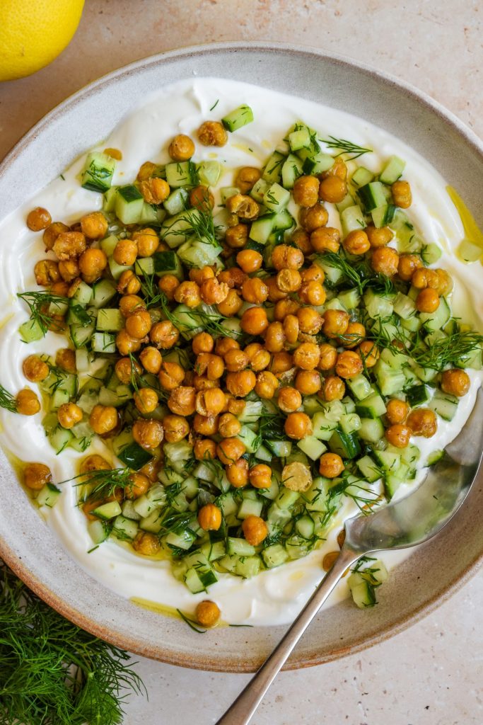 Bowl of dill and cucumber salad with crispy chickpeas on a bowl of Greek yogurt.