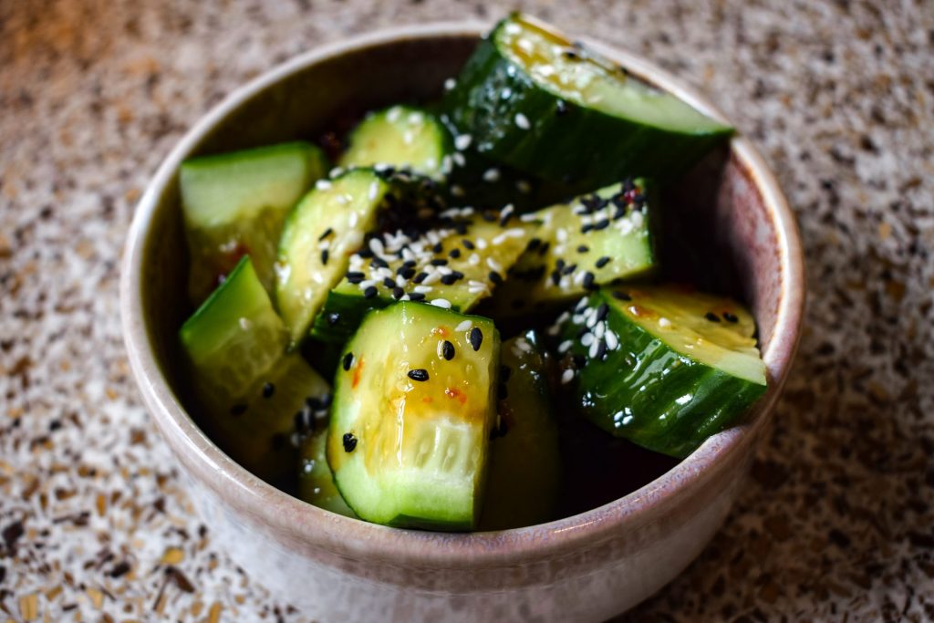 A close up of a bowl of Asian cucumber salad with sesame seeds and chilli.