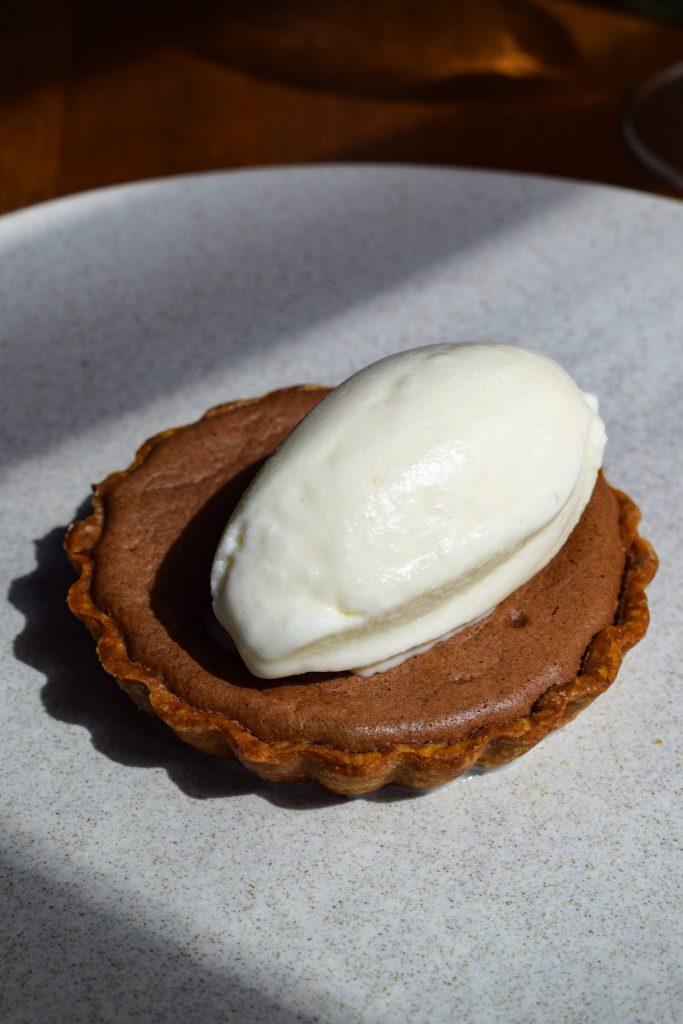 Chocolate tart topped with a quenelle of milk sorbet on a grey plate.