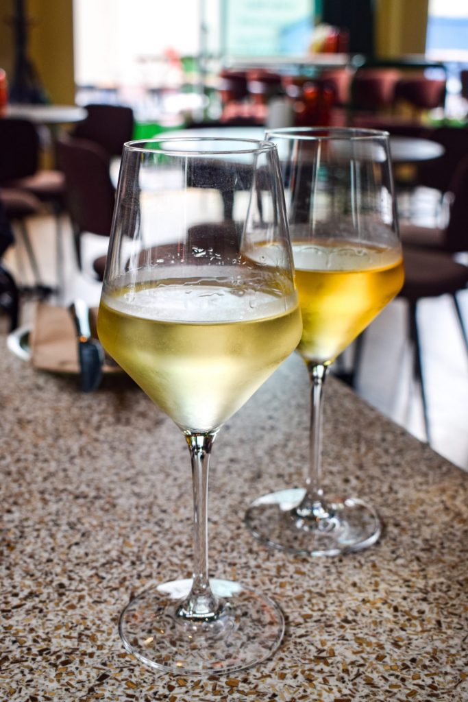 A glass of white wine and a glass of orange wine on a restaurant table.