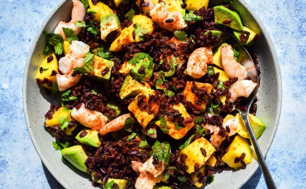Bowl of black rice, prawn, avocado and mango salad with chilli seasoning sprinkled on top.