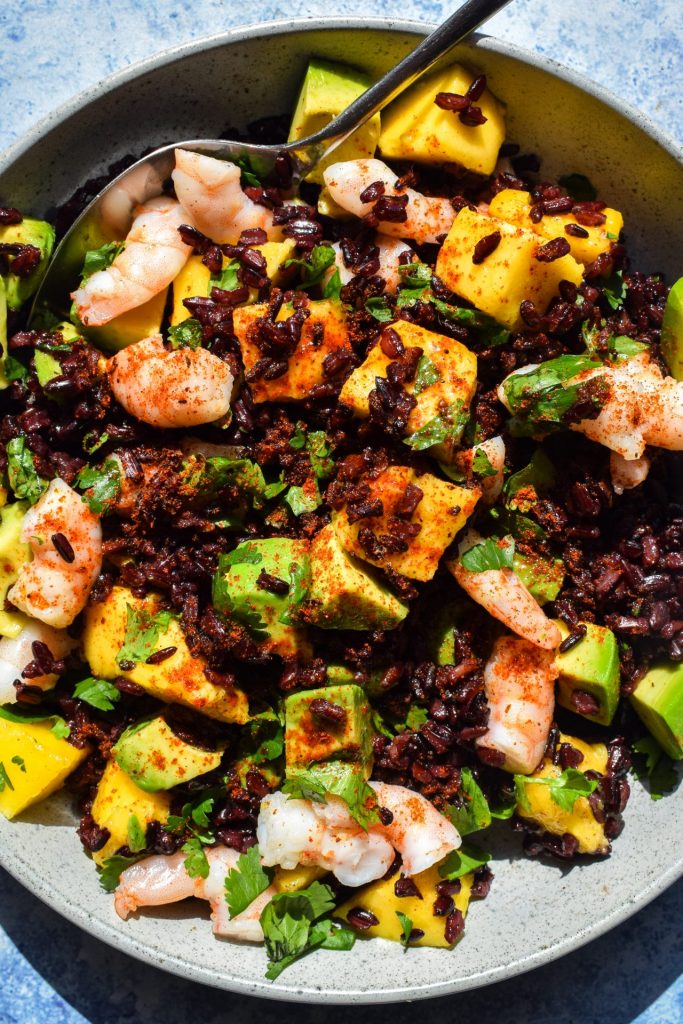 Close up of a bowl of black rice salad with prawns, mango and avocado.