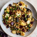 Grape and roasted cauliflower grain salad in a bowl with a bunch of grapes off to the side.