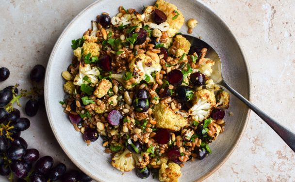 Grape and roasted cauliflower grain salad in a bowl with a bunch of grapes off to the side.
