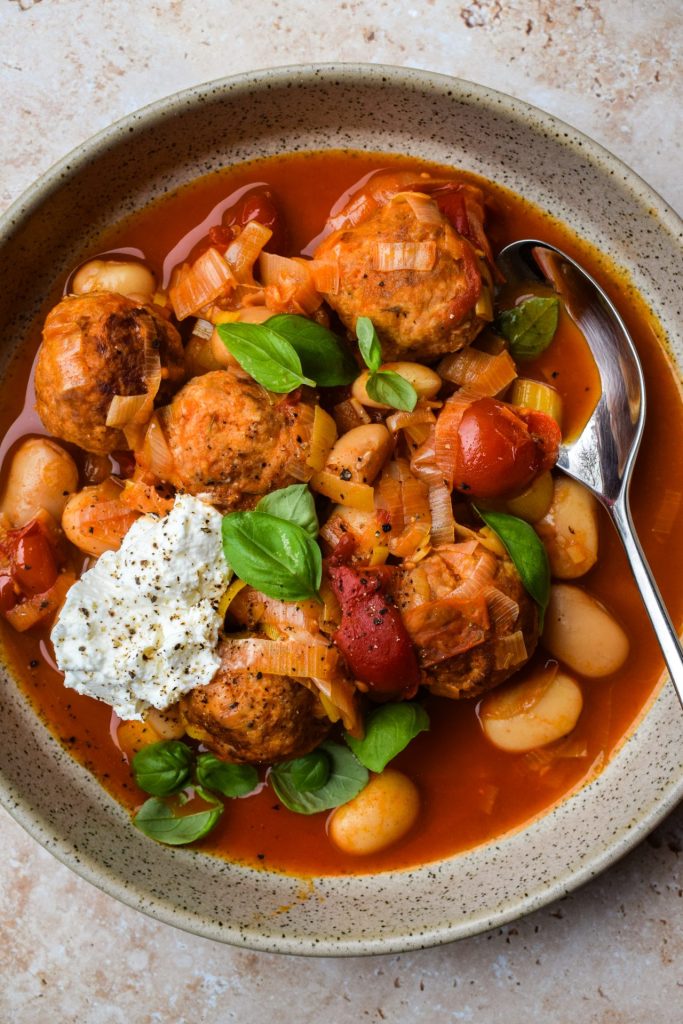 Close up of a bowl of butter beans, turkey meatballs, cherry tomatoes, basil and ricotta.